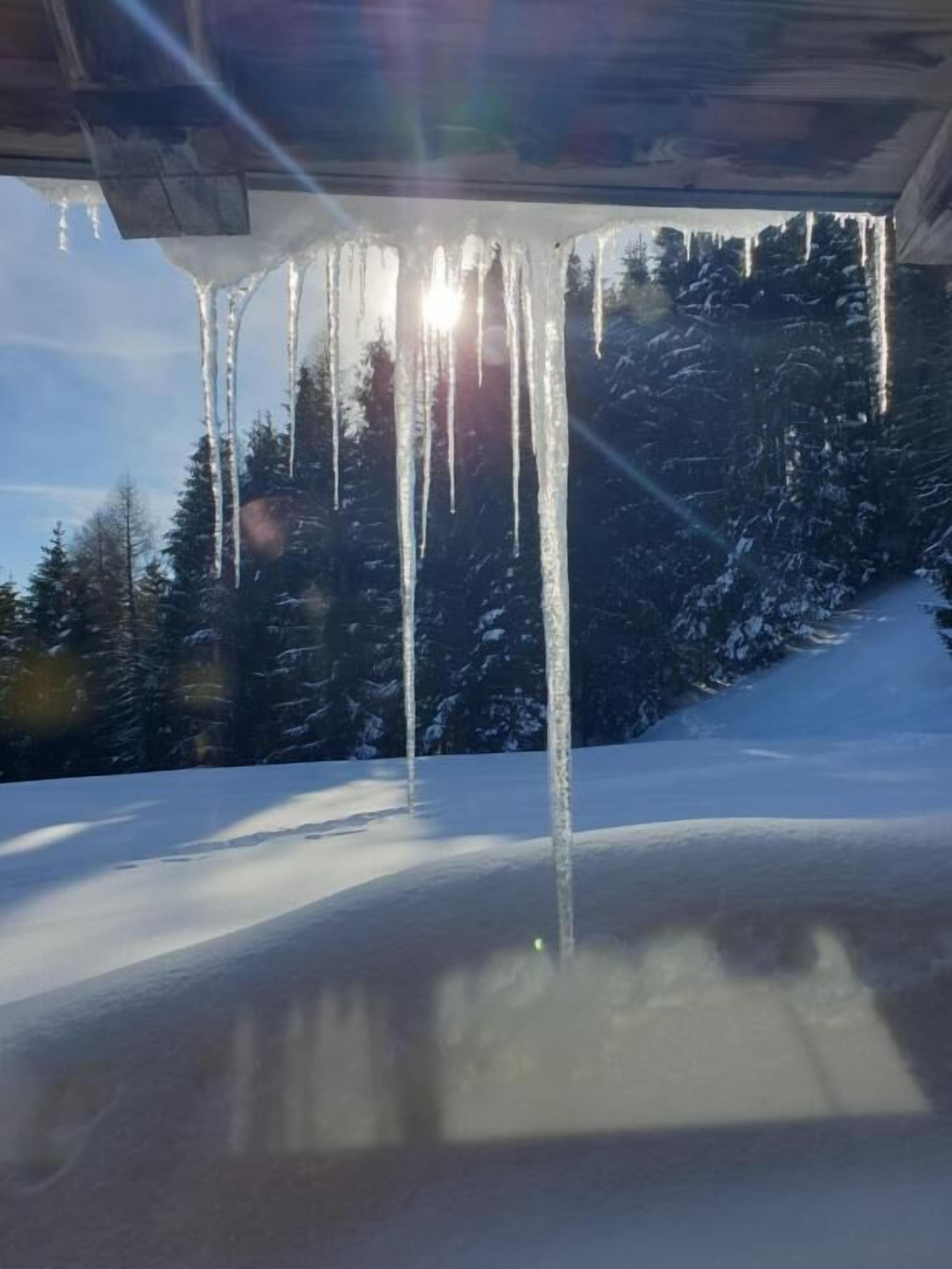 Des glaçons pendants d’un toit, un paysage enneigé et un ciel dégagé.