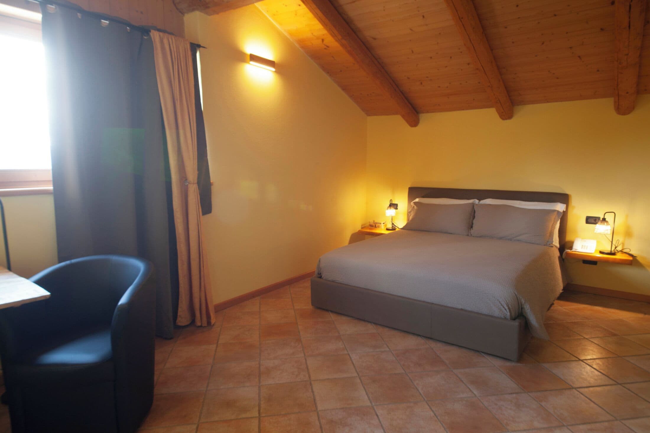 A bedroom with a bed, bedside lamps, a chair, and a window with curtains.