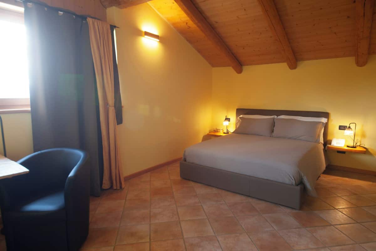 A bedroom with a bed, bedside lamps, a chair, and a window with curtains.