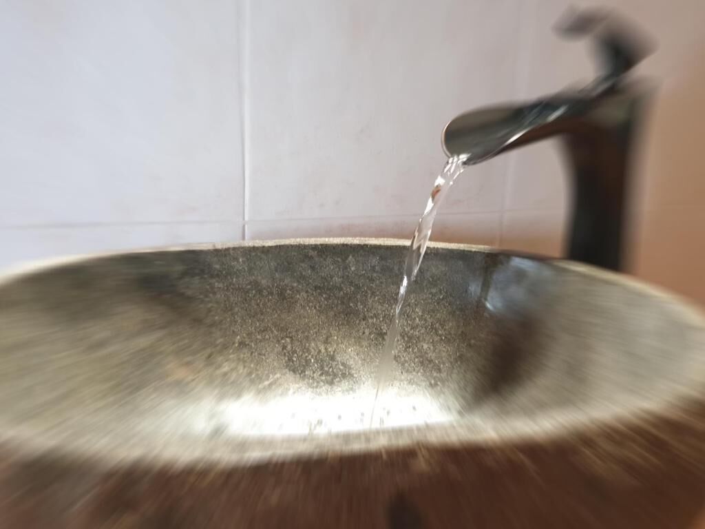 A metallic bowl with water being poured into it.