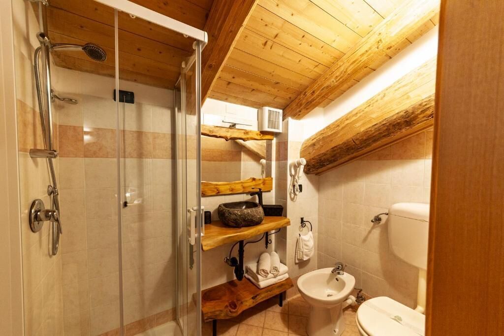 Une salle de bain avec une douche à parois de verre, des étagères en bois, un lavabo et des toilettes.