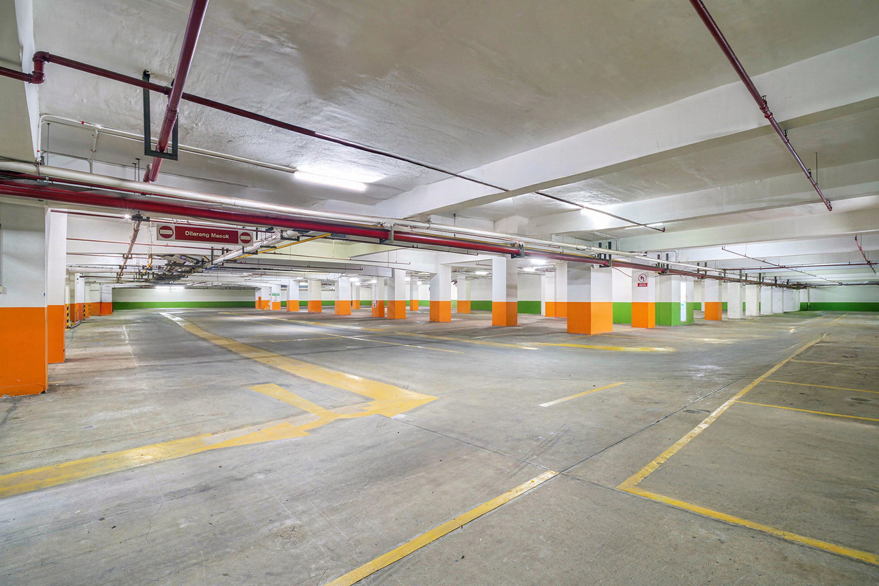 An indoor parking garage with concrete floors, orange and green pillars, and visible pipes on the ceiling.