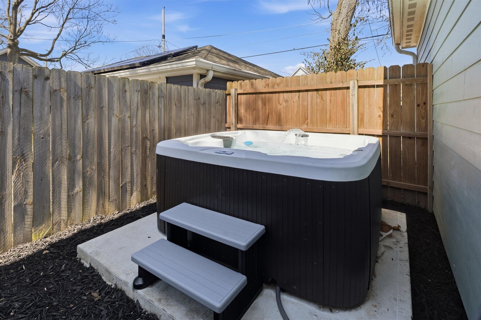 Een hottub met treden, omringd door een houten schutting en een huis.