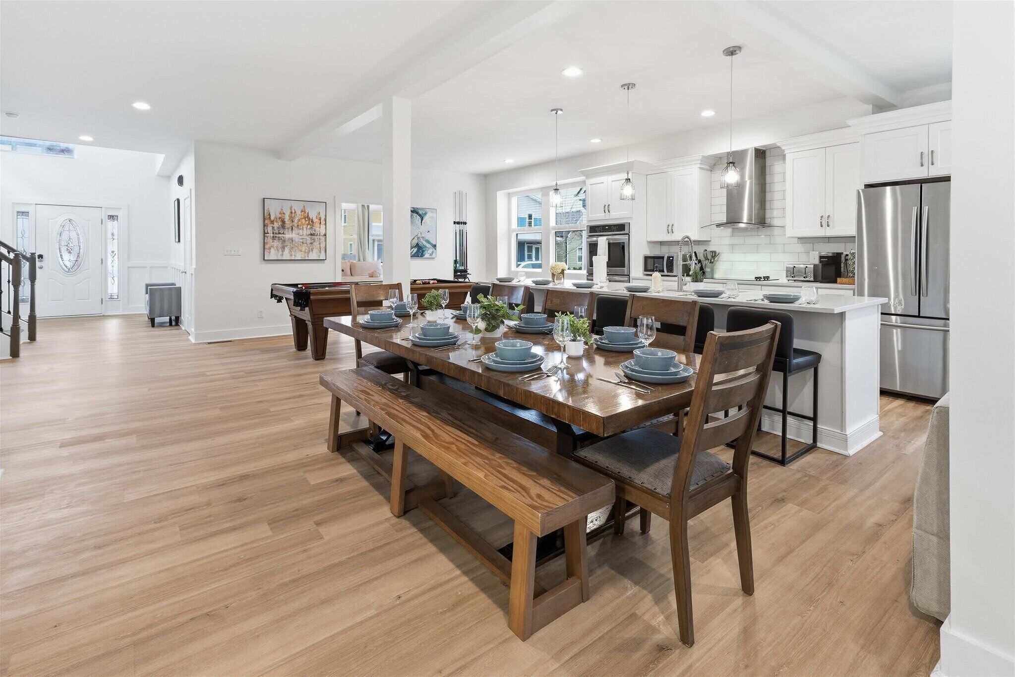 Une cuisine moderne dotée d’appareils électroménagers en acier inoxydable, un coin repas avec une table et des bancs en bois, et une vue sur le salon.
