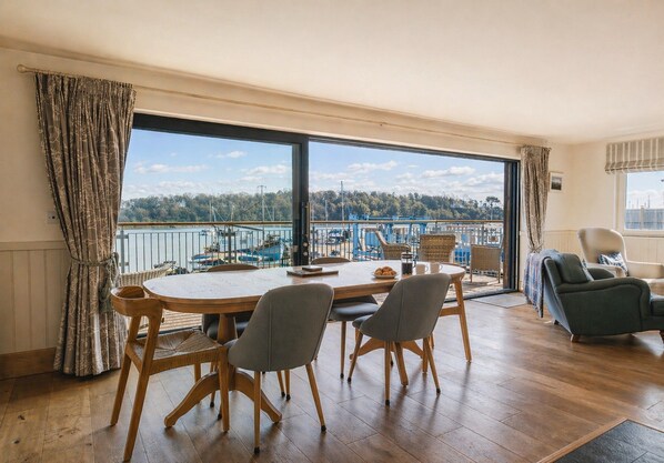 Un comedor con vista a un puerto deportivo, muebles de madera y un ventanal grande.