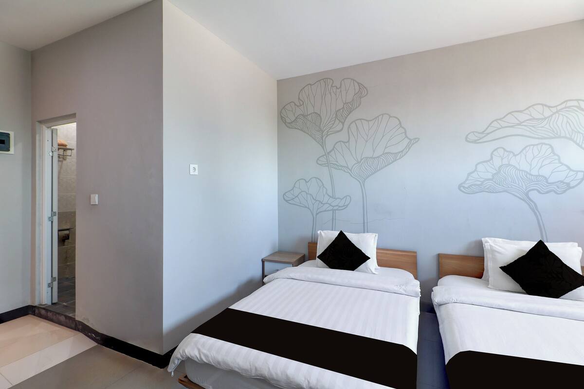 Une chambre d’hôtel avec deux lits, une porte de salle de bain et un mur orné d’un motif de feuilles.