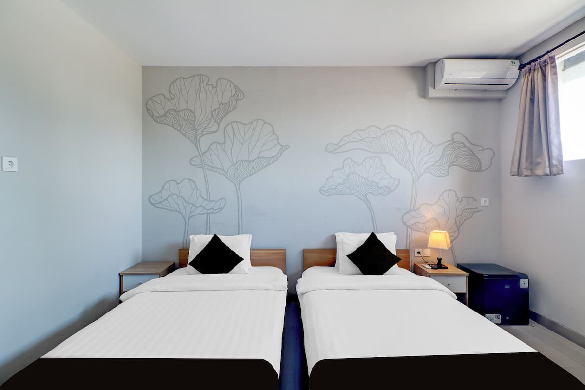 Habitación de hotel con dos camas, un mural en la pared, aire acondicionado, una mesita de noche con lámpara y una maleta.