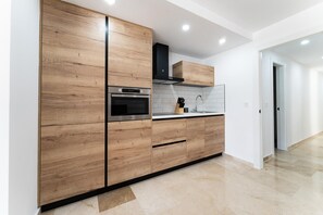 A modern kitchen with wooden cabinetry, stainless steel appliances, and a tiled backsplash. - Apartment With Pool in the Heart of Marbella (Marbella)