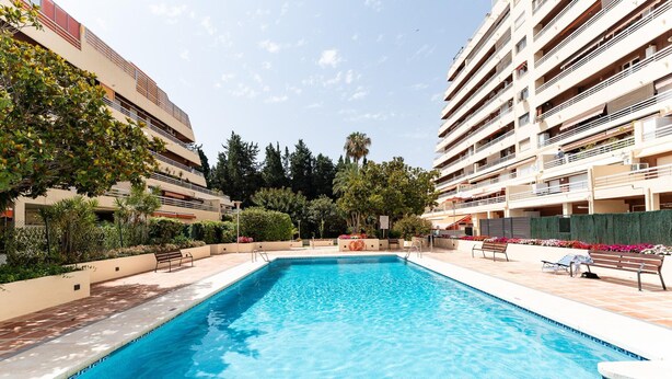 A swimming pool surrounded by a landscaped area with benches and a view of residential buildings. - Apartment With Pool in the Heart of Marbella (Marbella)