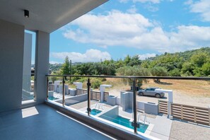 Een balkon met glazen hekwerk met uitzicht op een zwembad en een parkeerplaats.