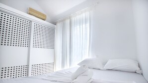 Ein Hotelzimmer mit Bett, weißen Vorhängen, einem Fenster und einer Wand-Klimaanlage.