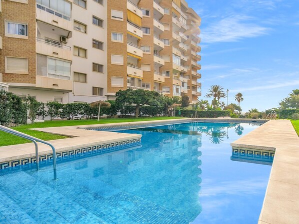 A swimming pool with a geometric tile pattern, surrounded by a low-rise building with balconies and a clear sky. - Sea View Apartment in Fuengirola (Fuengirola)