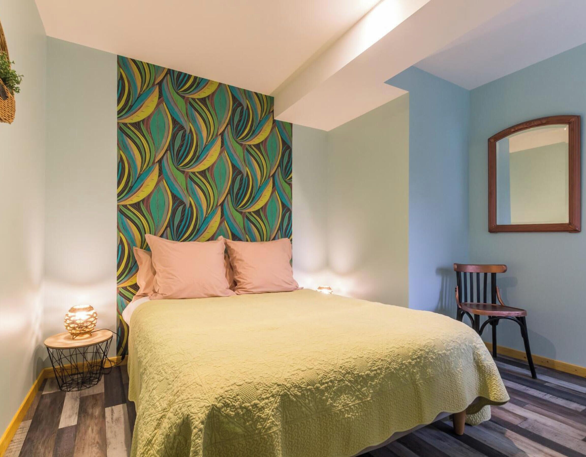 Un dormitorio con cabecera estampada, cama con manta texturizada, lámpara de noche y una silla.