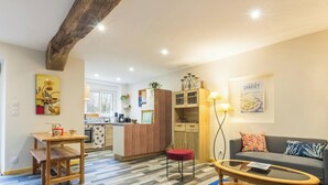 A modern living room with a sofa, a dining table, a kitchen area, and a wooden ceiling beam. - Peaceful country house - 4 guests (SAINT SAUVEUR VILLAGES)