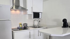 Ett modernt kök med vita skåp, en köksfläkt i rostfritt stål, en mikrovågsugn och en vattenkokare på bänkskivan.
