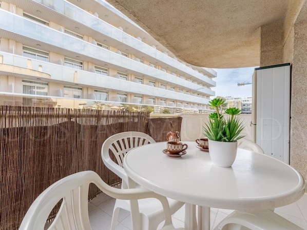 A balcony with a round table, white chairs, a potted plant, and a decorative pitcher. - Renovated apartment central Salou - 4 guests (Salou)