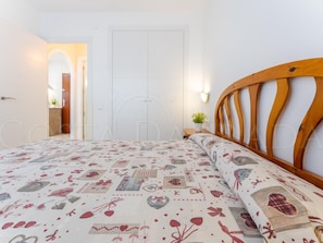 Une chambre à coucher comprenant un lit, une tête de lit en bois, une table de chevet, une lampe fixée au mur et une porte.