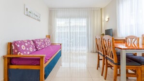 Una habitación con sofá, una mesa de comedor con sillas, un televisor y una ventana con cortinas.