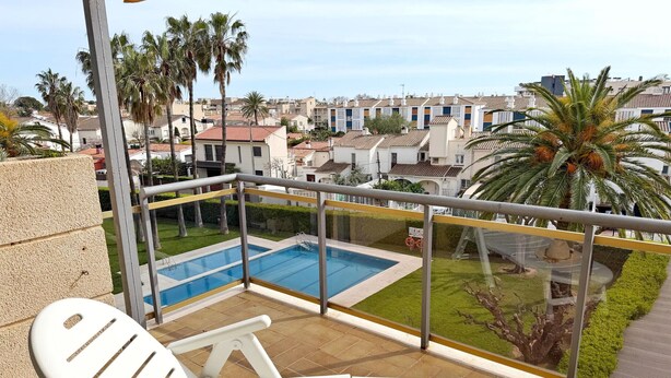 En balkon med pool, hvide stole og udsigt til boligbygninger og palmer.
