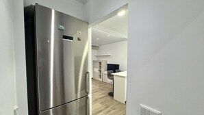 Een moderne keuken met een roestvrijstalen koelkast, een eethoek met een witte tafel en stoelen, en een licht houten vloer.