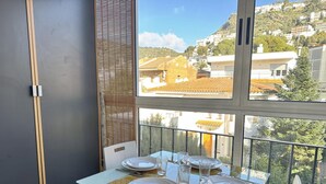 Een balkon met een eettafel, met uitzicht op een woonwijk met huizen en een heuvel.