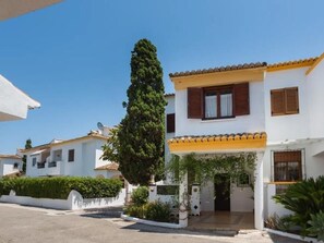 Un edificio residencial con fachada blanca, techo de tejas y un árbol grande en el frente.