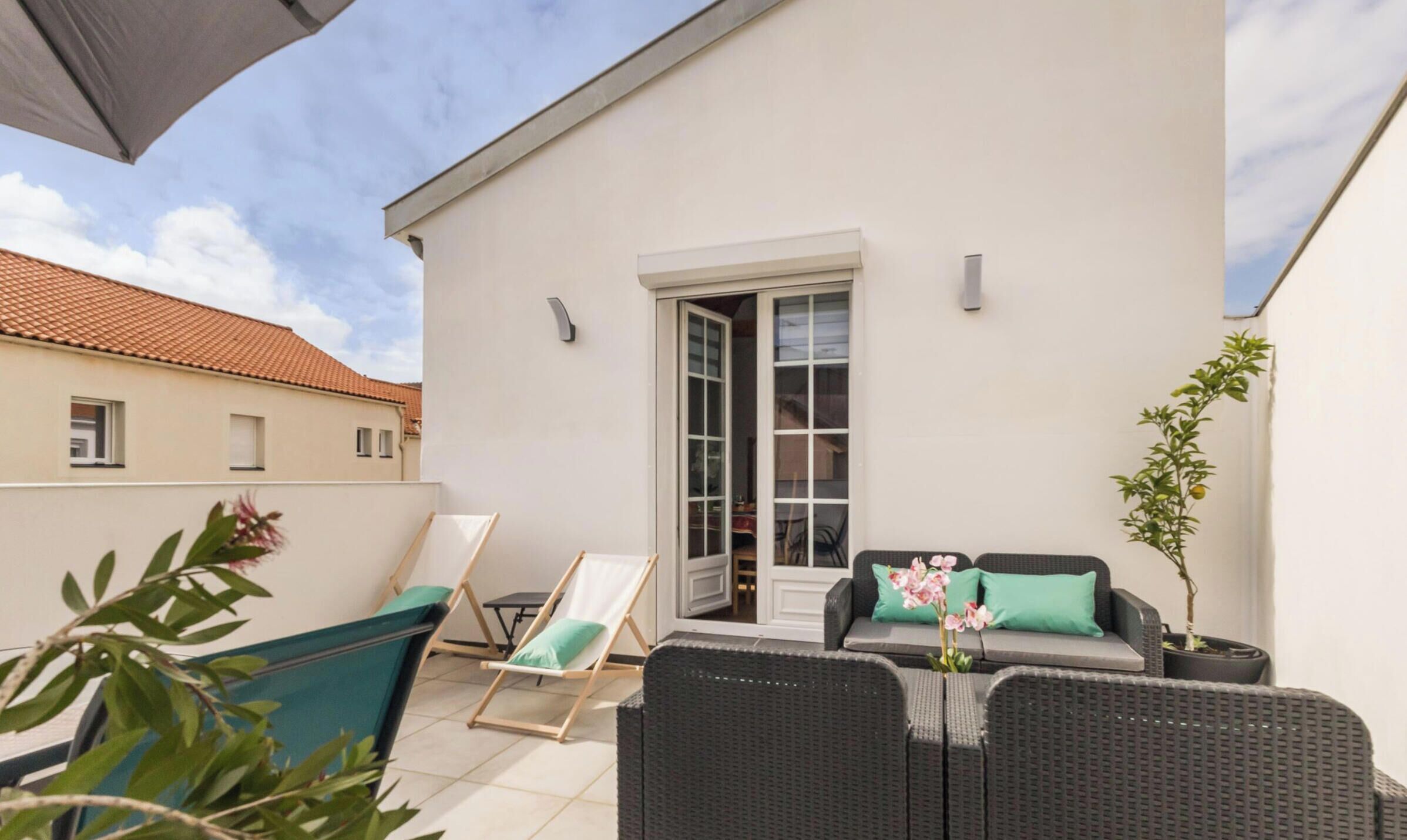Ein Balkon mit Korbmöbeln, einem Blumentopf und einer Tür zu einem Innenraum.