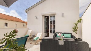 Un balcon agrémenté de meubles en osier, d’une plante en pot et d’une porte donnant sur un espace intérieur.