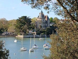 Ein schlossartiges Gebäude mit einem Turm, umgeben von einem Gewässer mit mehreren Segelbooten.