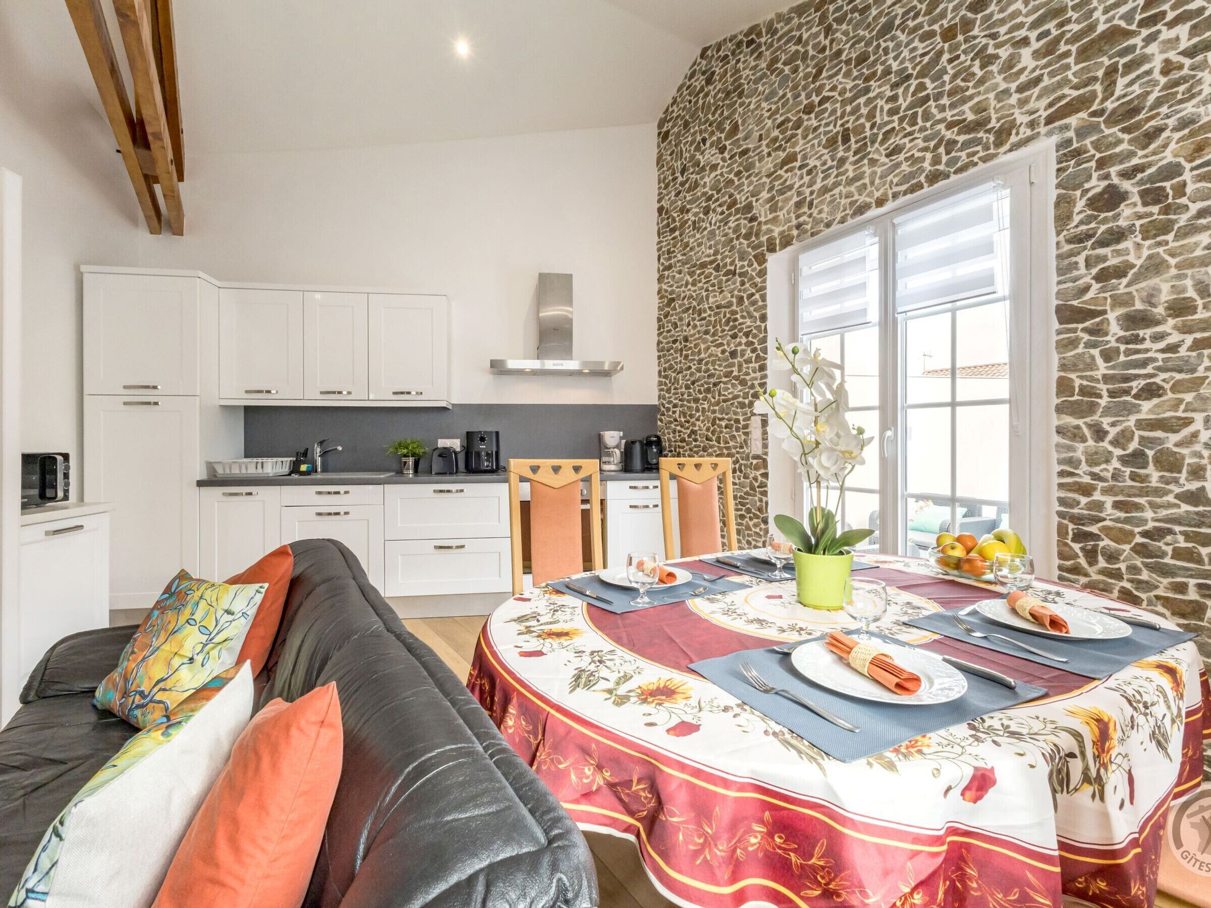 A modern kitchen with white cabinets, a stone wall, and a dining area with a table set for two.