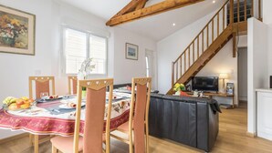 Un coin repas avec une table dressée pour quatre personnes, un canapé, un escalier et un téléviseur en arrière-plan.