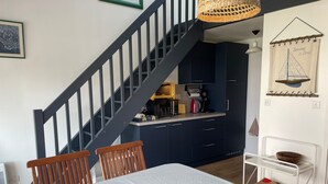 A dining area with a table, chairs, a staircase, and a kitchen area in the background. - Bright apartment near the beach - 6 guests (Arzon)