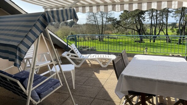 A covered outdoor seating area with a table and chairs, overlooking a grassy landscape with trees. - Bright apartment near the beach - 6 guests (Arzon)