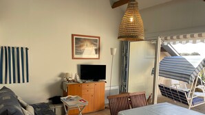 A living room with a sofa, a table, a TV, a cabinet, and a hanging light fixture. - Bright apartment near the beach - 6 guests (Arzon)