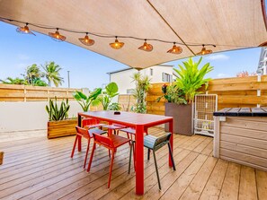 Une terrasse extérieure avec une plateforme en bois, une table rouge avec des chaises et des guirlandes lumineuses.