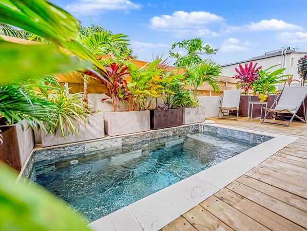 Une piscine avec une terrasse en bois et des plantes en pot.