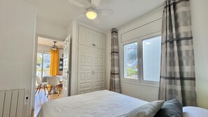 A bedroom with a bed, a ceiling fan, a window with curtains, and a door leading to a balcony. - Cozy Apartment with Pool and Terrace in Puig Rom, 2km from Roses Beach - Sleeps 4 (Roses)