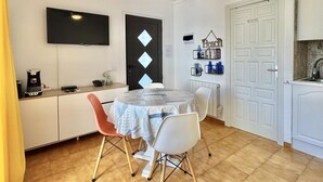 A dining area with a round table, two chairs, a ceiling fan, a TV, and a door with a 'NO FLAMMABLE' sign. - Cozy Apartment with Pool and Terrace in Puig Rom, 2km from Roses Beach - Sleeps 4 (Roses)