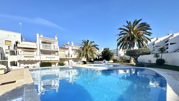 A swimming pool surrounded by white buildings with balconies, palm trees, and a clear blue sky. - Cozy Apartment with Pool and Terrace in Puig Rom, 2km from Roses Beach - Sleeps 4 (Roses)
