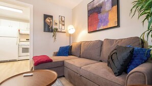 En stue med sofa, sofabord og lampe. Et køkken er synligt i baggrunden.