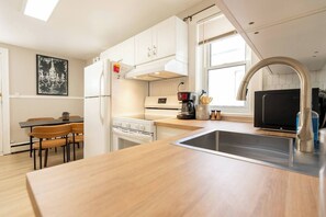 A compact kitchen with white cabinets, a dining area with wooden chairs, a coffee maker, and a microwave.