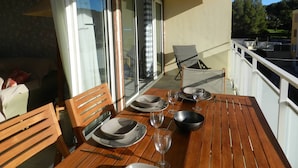 A balcony with a table set for dining, chairs, and a view of the outdoors. - Apartment, AC, parking - 4 guests (Bormes-les-Mimosas)