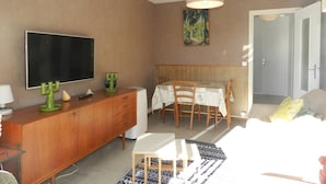 A room with a television, a wooden cabinet, a dining table with chairs, a bed, and a painting on the wall. - Apartment, AC, parking - 4 guests (Bormes-les-Mimosas)