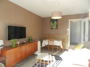 Ein Zimmer mit Fernseher, Holzschrank, Esstisch mit Stühlen, Bett und einem Bild an der Wand.
