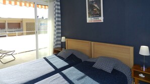 A hotel room with a bed, a poster on the wall, a window with curtains, and a view of the outside. - Apartment, AC, parking - 4 guests (Bormes-les-Mimosas)