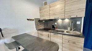 A compact kitchen with a dark countertop, wooden cabinets, a built-in stove, and a sink. - Studio near the beach - 2 guests (Cap d'Agde)