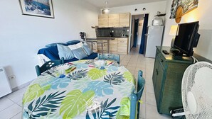 A compact living space with a bed, a dining table, a kitchenette, a TV, and a fan. - Studio near the beach - 2 guests (Cap d'Agde)