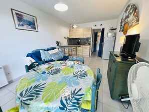 Ein kompakter Wohnbereich mit Bett, Esstisch, Küchenzeile, Fernseher und Ventilator.