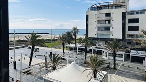 A view of a coastal building with a beach in the background, palm trees, and a pizzeria sign. - Studio near the beach - 2 guests (Cap d'Agde)