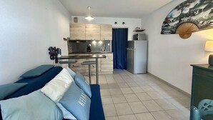 A compact living space with a kitchenette, a sofa with pillows, a dining area, and a painting on the wall. - Studio near the beach - 2 guests (Cap d'Agde)